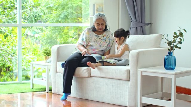 elderly female reading book with little granddaughter on couch