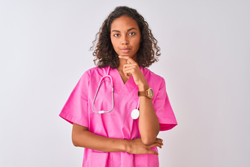 Young brazilian nurse woman wearing stethoscope standing over isolated white background looking confident at the camera with smile with crossed arms and hand raised on chin. Thinking positive.