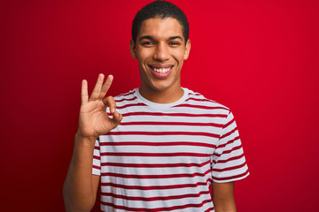Young handsome arab man wearing striped t-shirt over isolated red background smiling positive doing ok sign with hand and fingers. Successful expression.