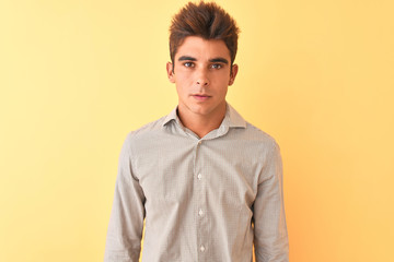 Young handsome man wearing casual shirt standing over isolated yellow background with serious expression on face. Simple and natural looking at the camera.