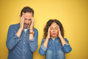 Beautiful middle age couple together standing over isolated yellow background with hand on headache because stress. Suffering migraine.
