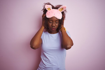 Young african afro woman wearing sleep mask standing over isolated pink background suffering from headache desperate and stressed because pain and migraine. Hands on head.