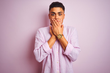 Young brazilian man wearing shirt standing over isolated pink background shocked covering mouth with hands for mistake. Secret concept.