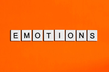 A homemade wooden tile with letters on a orange background, word emotions