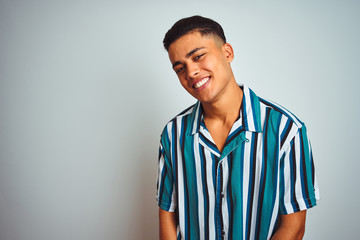 Young brazilian man wearing summer striped shirt standing over isolated white background looking away to side with smile on face, natural expression. Laughing confident.