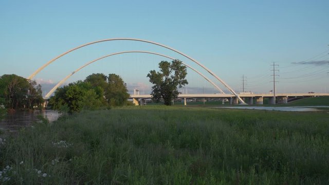 4K - The Margaret McDermott Bridge is seen in the distance as traffic drives by. Grass is in the foreground.