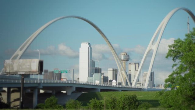 4K - Slow ZOOM-IN - The Dallas Skyline is Framed by the Margaret McDermott Bridge with the Iconic Reunion Tower in the center. Slow moving traffic drives over the bridge on a beautiful day.