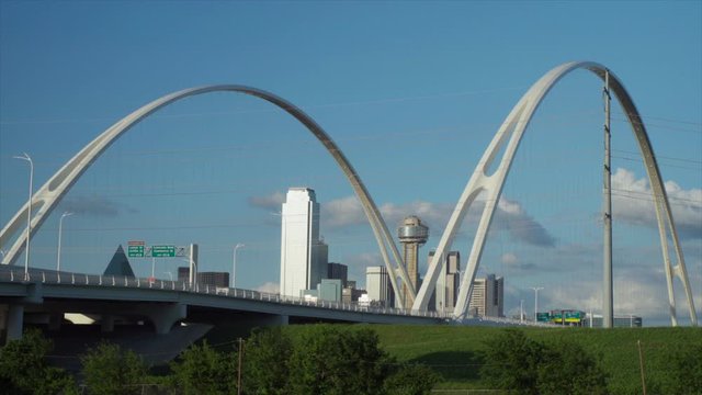 The Dallas Skyline is Framed by the 2 Arches of the Margaret McDermott Bridge with the Iconic Reunion Tower in the center. Slow moving traffic drives over the bridge on a beautiful day. Wide - 1080p