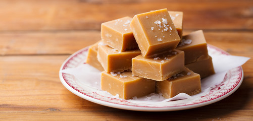 Caramel fudge candies on a plate. Wooden background. Close up.