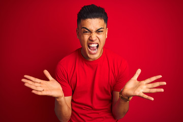 Naklejka premium Young brazilian man wearing t-shirt standing over isolated red background celebrating crazy and amazed for success with arms raised and open eyes screaming excited. Winner concept