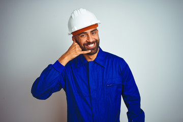 Handsome indian worker man wearing uniform and helmet over isolated white background smiling doing phone gesture with hand and fingers like talking on the telephone. Communicating concepts.