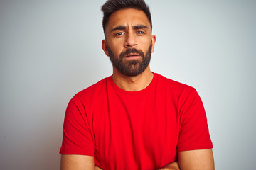 Young indian man wearing red t-shirt over isolated white background skeptic and nervous, disapproving expression on face with crossed arms. Negative person.