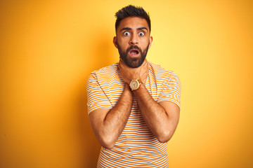 Young indian man wearing t-shirt standing over isolated yellow background shouting suffocate because painful strangle. Health problem. Asphyxiate and suicide concept.