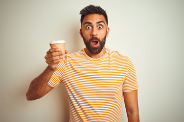 Young indian man drinking cup of coffee standing over isolated white background scared in shock with a surprise face, afraid and excited with fear expression