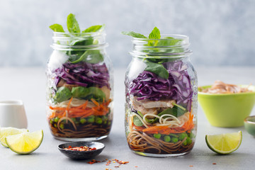 Healthy asian salad with noodles, vegetables, chicken and tofu in glass jars. Grey background. - obrazy, fototapety, plakaty