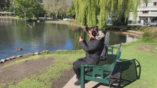 Young woman filming lake during cold sunny day in Beacon Hill Park, Canada
