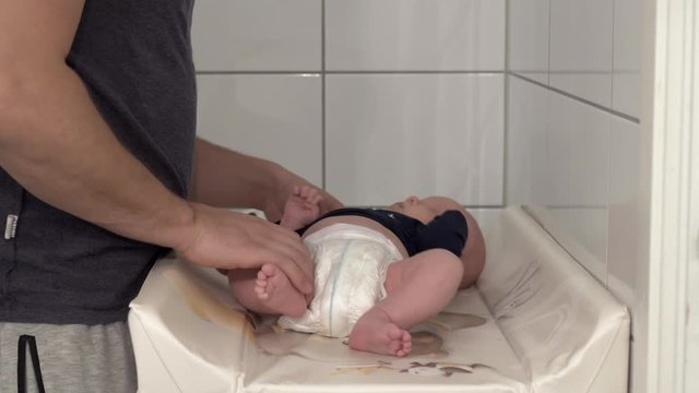 Father carefully dressing his newborn baby boy on baby changing table unit.