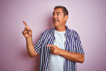 Handsome middle age man wearing striped shirt standing over isolated pink background smiling and looking at the camera pointing with two hands and fingers to the side.