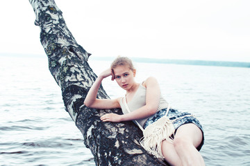 young blond woman hanging on birch tree at lake shore, summer vacations outdoor lifestyle