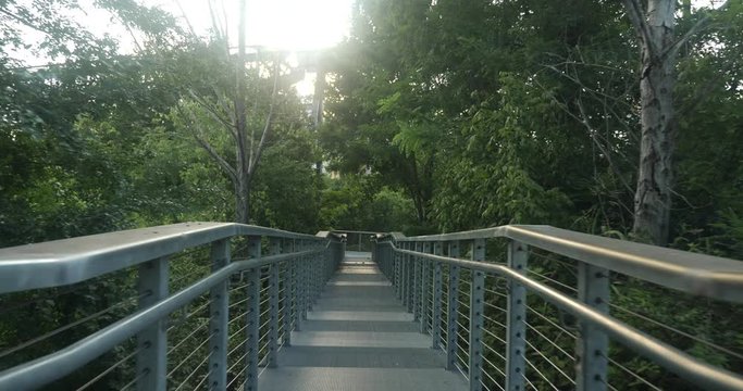 POV walking down a bridge on a path in a park