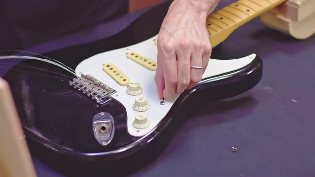 Luthier unscrewing pickguard and shows electrical components of guitar
