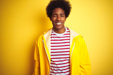 African american man with afro hair wearing rain coat standing over isolated yellow background...