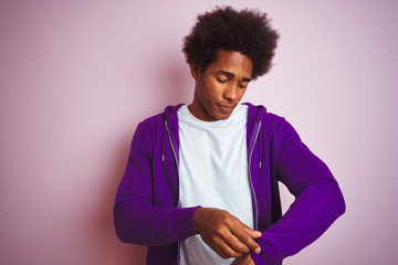 Young african american man wearing purple sweatshirt standing over isolated pink background amazed and surprised looking up and pointing with fingers and raised arms.