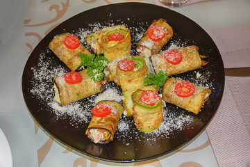 Vegetarian rolls with squash, tomato, cheese and greenery on black plate.