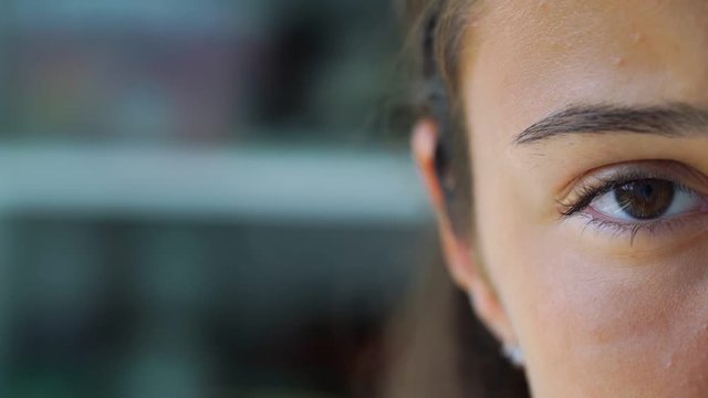 girl teenager face part with blinking multiple times brown eye looking ahead on blurry background extreme close view