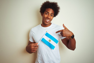 Afro american tourist man holding Argentinian Argentina flag over isolated white background with surprise face pointing finger to himself