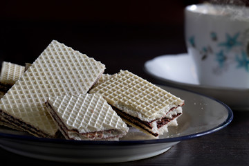 Wafer stuffed chocolate in white dish and tea bag in hot water in the white cup