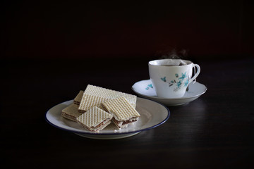 Wafer stuffed chocolate in white dish and tea bag in hot water in the white cup