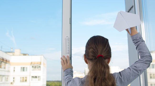 child girl, rear view, releases a paper plane from a plastic window, against the sky, close-up