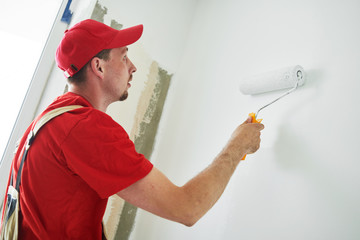 Painter worker with roller painting wall surface into white