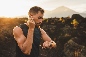Male runner synchronizing wireless earphones with smart watch. Preparing for trail running outdoors...