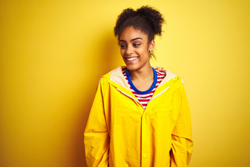 Obraz na płótnie Canvas Young african american woman wearing rain coat over isolated yellow background looking away to side with smile on face, natural expression. Laughing confident.