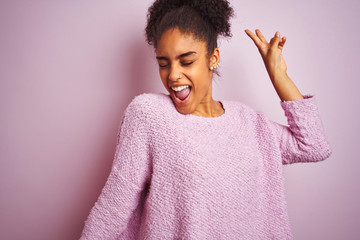 Young african american woman wearing winter sweater standing over isolated pink background Dancing happy and cheerful, smiling moving casual and confident listening to music