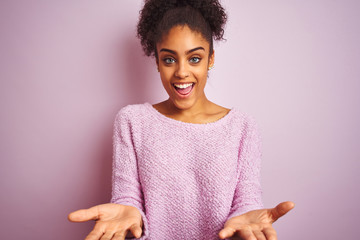 Young african american woman wearing winter sweater standing over isolated pink background smiling cheerful offering hands giving assistance and acceptance.