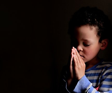 boy praying to God stock image with hands held together with closed eyes