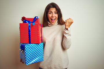 Young beautiful woman holding birthday gifts standing over isolated white background screaming proud and celebrating victory and success very excited, cheering emotion