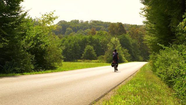 A man travelling with a touring bicycle through the forest road.