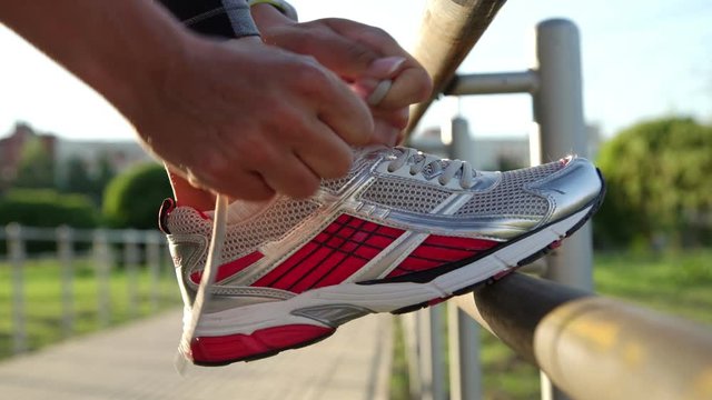 sporty lady in leggings puts foot on metal handrail and ties fashionable sneaker laces and starts running close view
