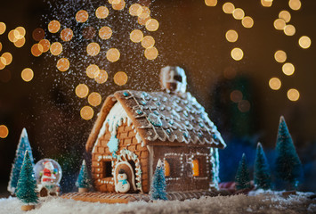 Traditional Christmas gingerbread house with snowfall on garland lights background