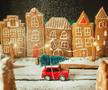 Toy car with Christmas tree in the gingerbread town during sugar snowfall
