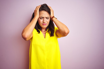 Young beautiful woman wearing yellow t-shirt standing over pink isolated background suffering from headache desperate and stressed because pain and migraine. Hands on head.