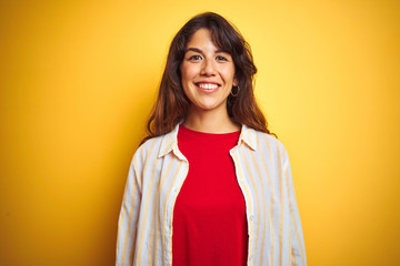 Young beautiful woman wearing red t-shirt and stripes shirt over yellow isolated background with a happy and cool smile on face. Lucky person.