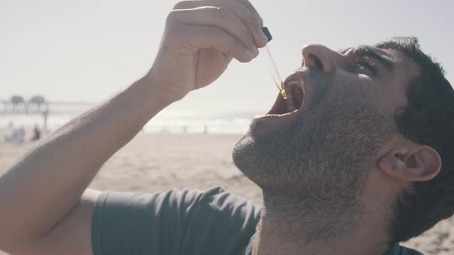 Young man taking tincture medicine with dropper at beach 