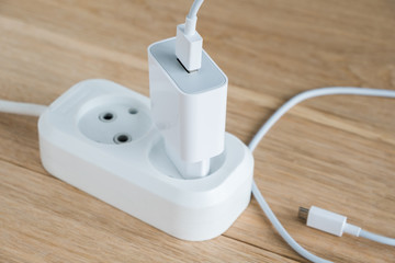 Charger with usb cable for smartphones connected to a power strip. Wood background.