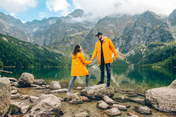 man with woman in yellow raincoat at sunny autumn day looking at lake in tatra mountains