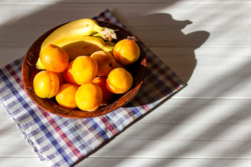 Bananas and apricots lie in a plate on a white table.